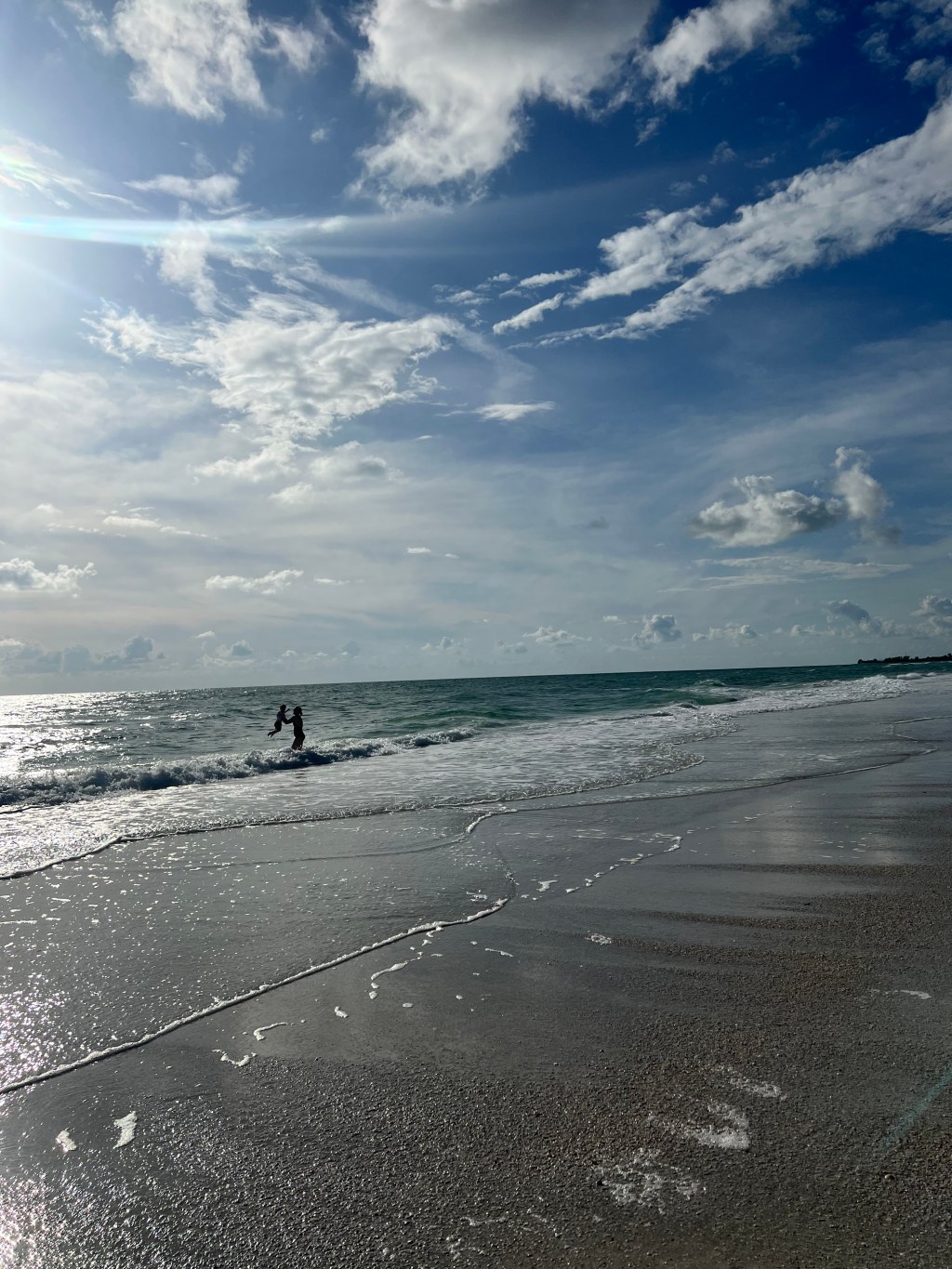 Mother and son exploring the beach together beside rolling waves and reflective sand.