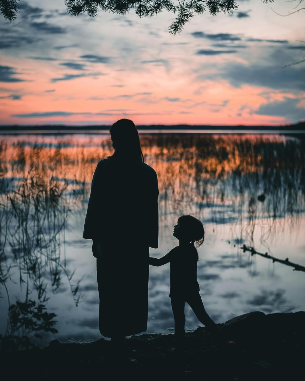 Silhouette of a mother standing beside a lake at sunset, reflecting the identity transformation and emotional growth of matrescence.