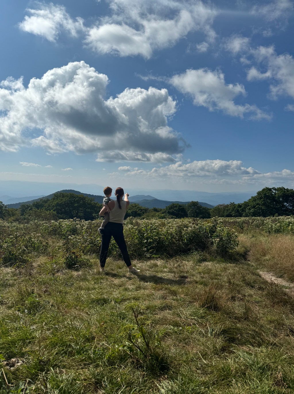 Mother holding her young child while overlooking the Blue Ridge Mountains beneath a wide sky.