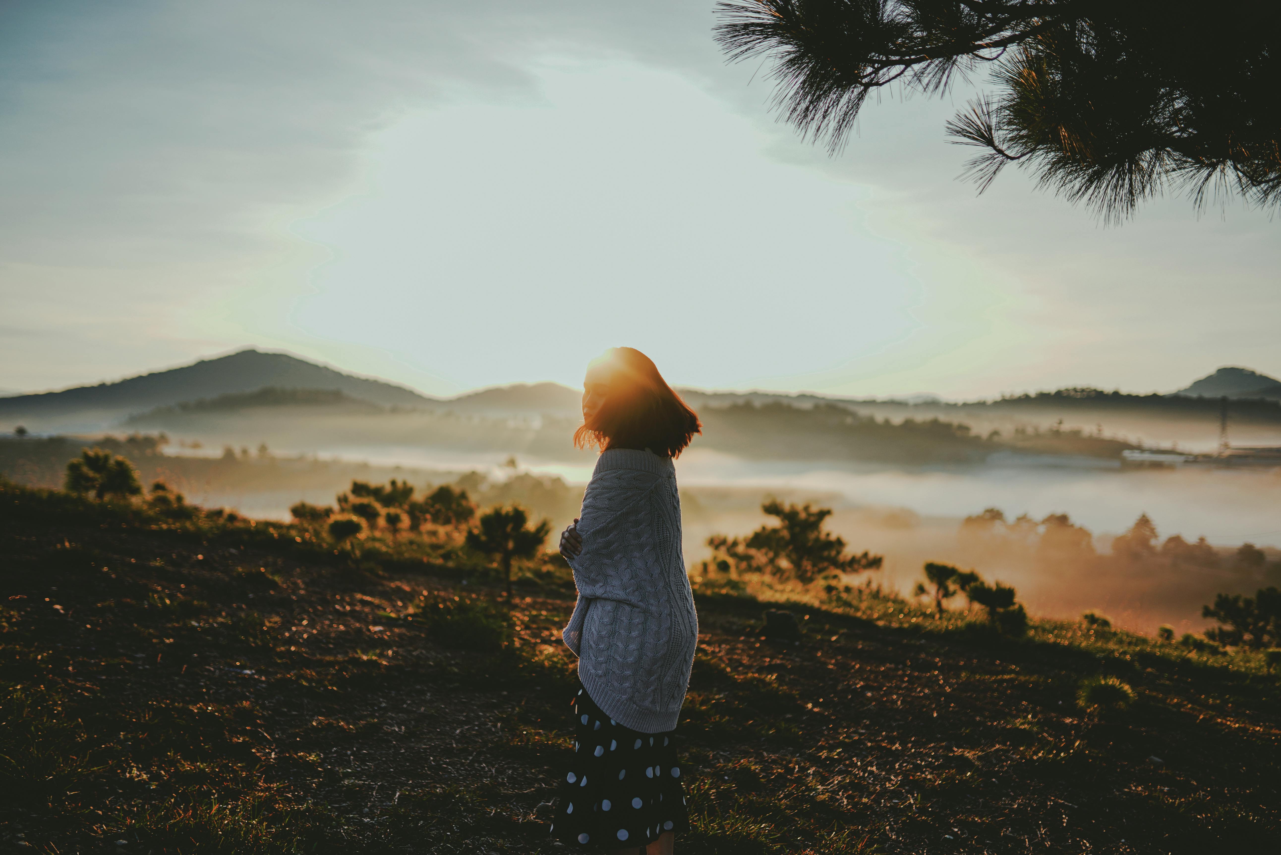 Woman standing in a misty mountain landscape at sunrise, reflecting on presence, awareness, and conscious living.