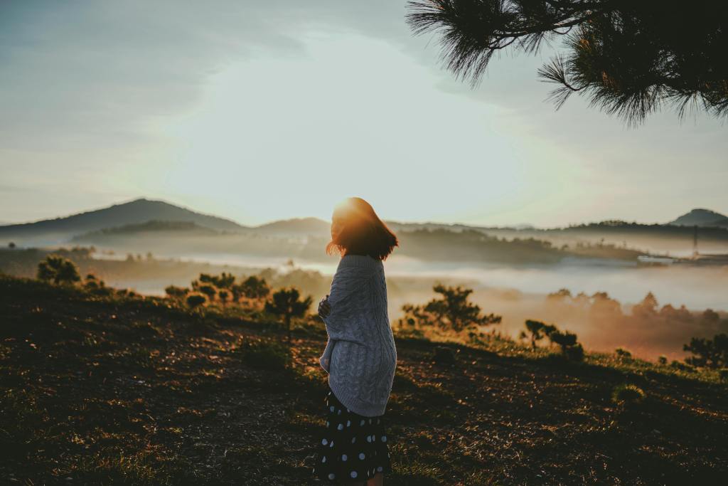 Woman standing in a misty mountain landscape at sunrise, reflecting on presence, awareness, and conscious living.